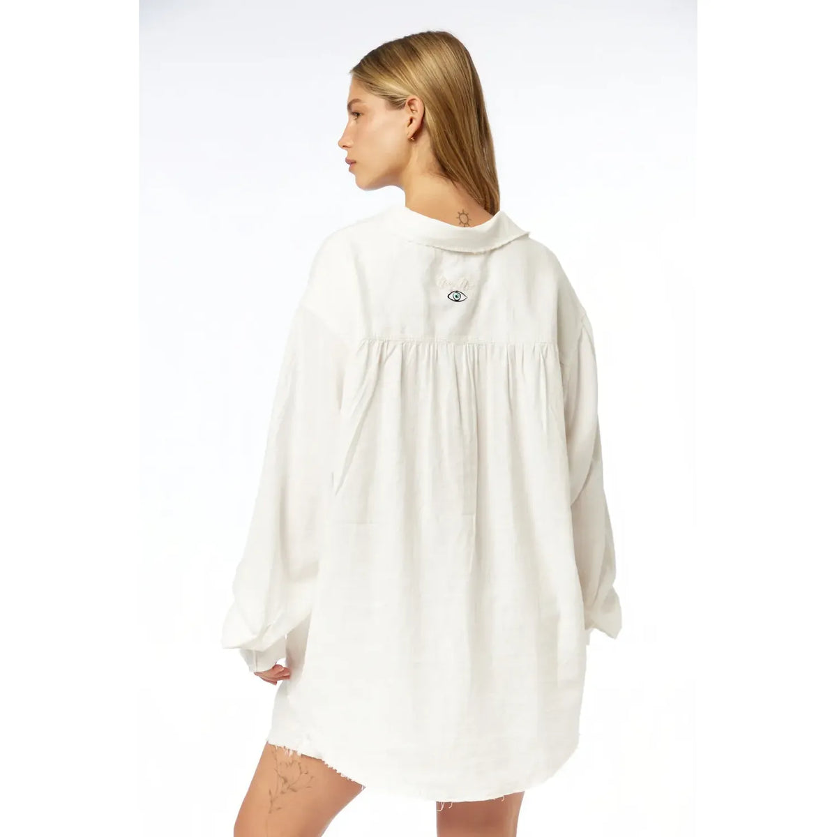 Back of a woman wearing an oversized white linen button-down shirt with an embroidered eye design on the upper back