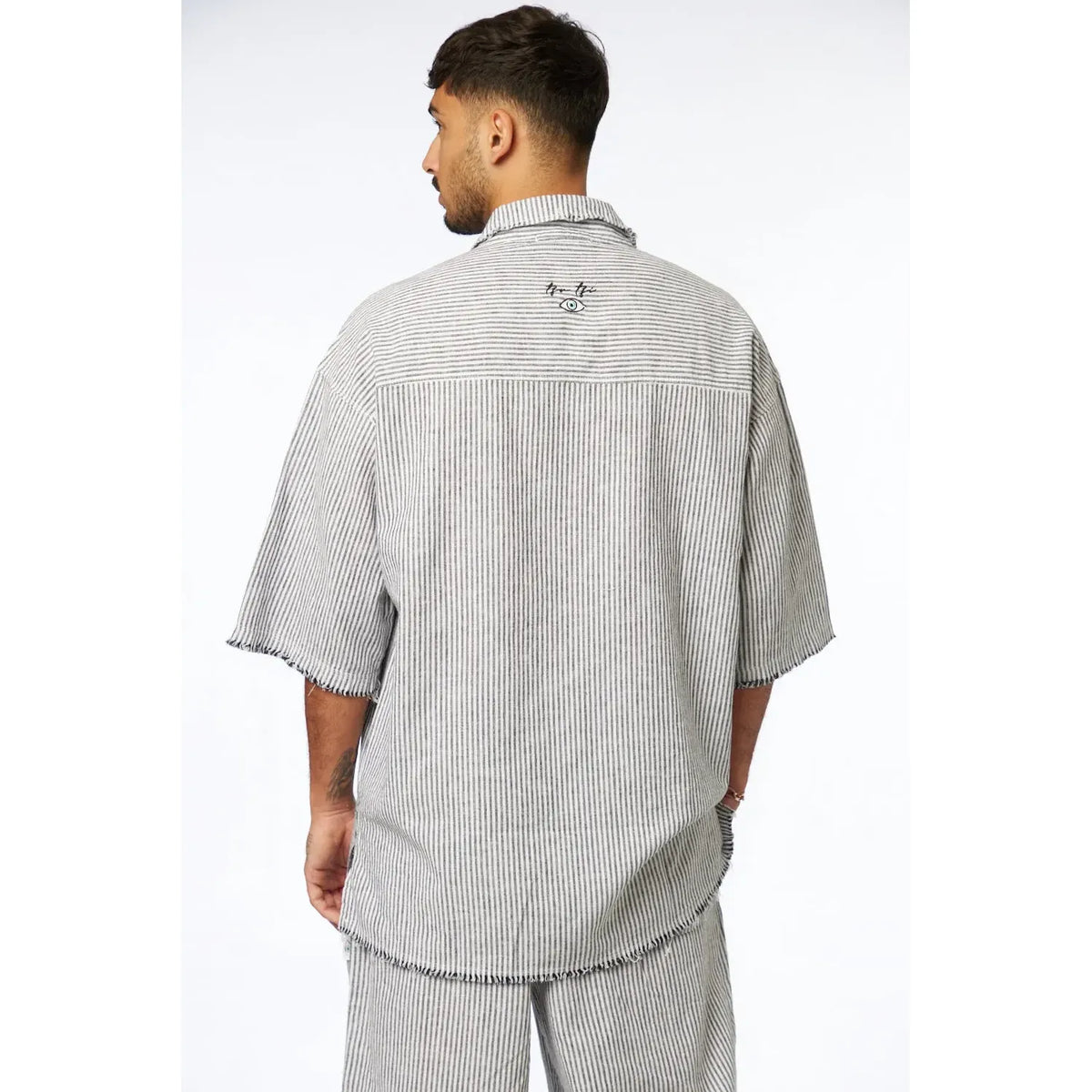 Man from behind wearing a black striped linen short sleeve button-up shirt with an eye graphic on the back