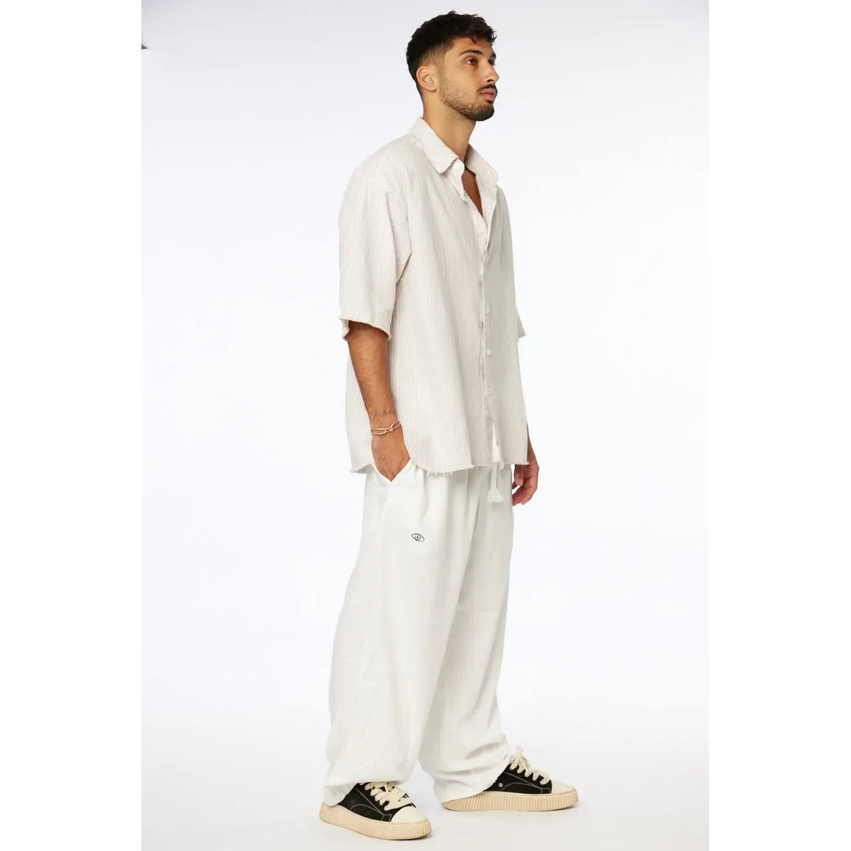 Man wearing a Striped Linen Short Sleeve Button-Up Shirt in Stone with white pants and black and white sneakers