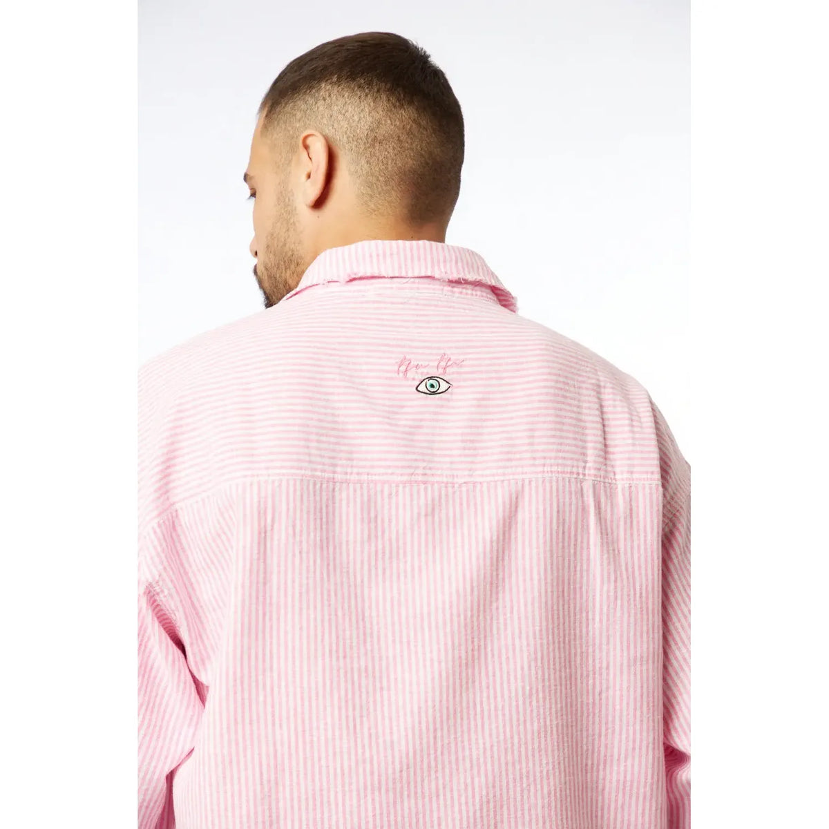 Back of a man wearing a pink striped linen short sleeve button-up shirt with an embroidered eye graphic