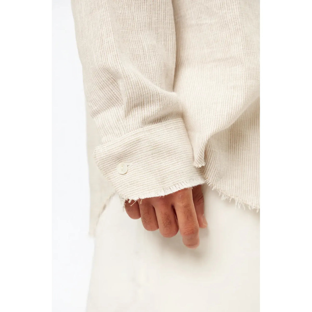 Close up of a person's hand wearing a Striped PURE Long Sleeve Linen Button-Up Shirt in Stone, showing the frayed cuff and button