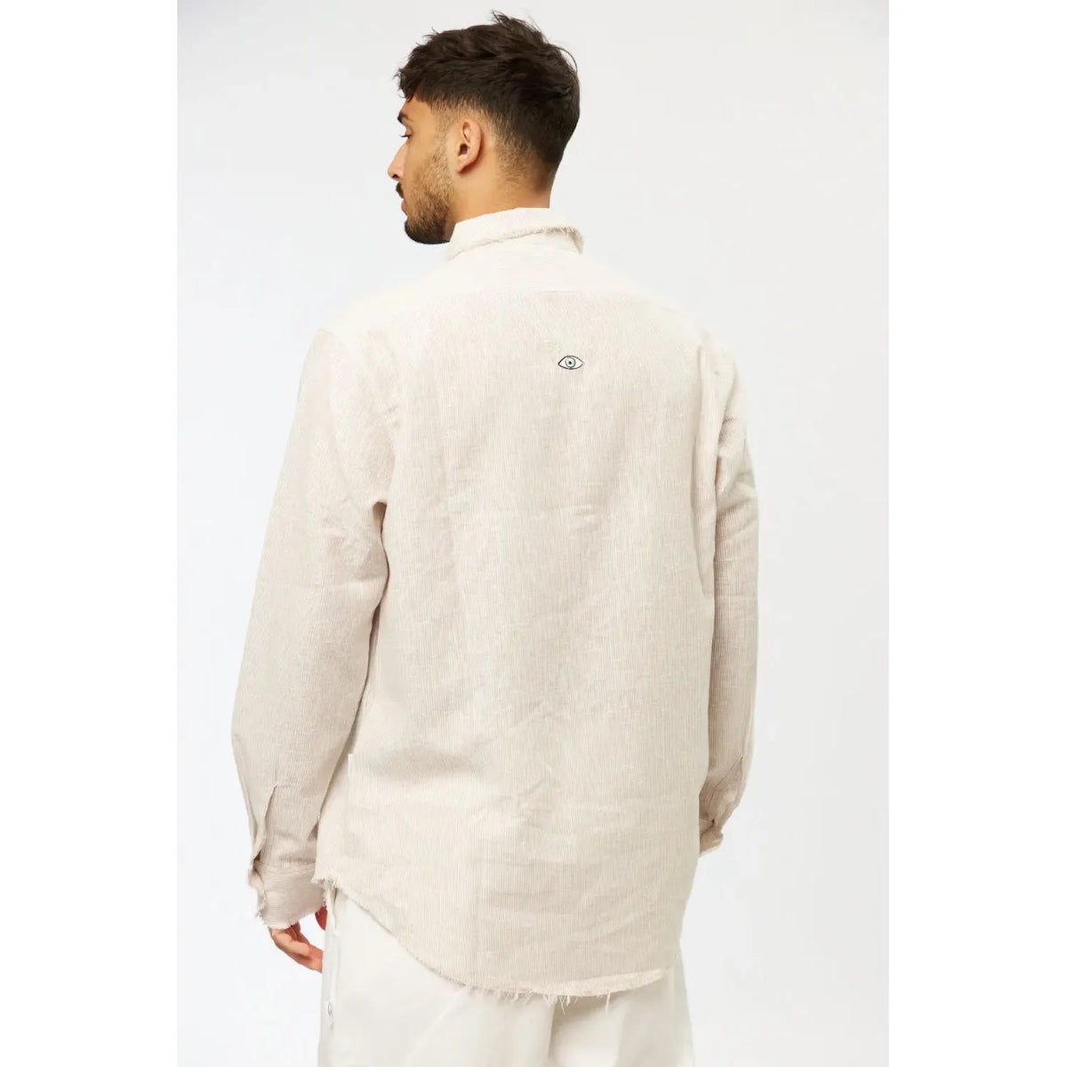 Back of a man wearing a Striped PURE Long Sleeve Linen Button-Up Shirt in Stone, with an eye graphic on the upper back