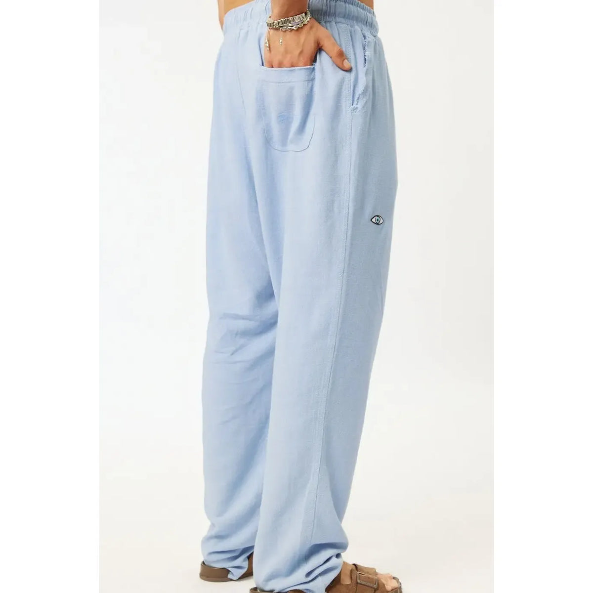 SOFT SL Linen Pants in sky blue, with a hand in the back pocket and an eye logo on the side