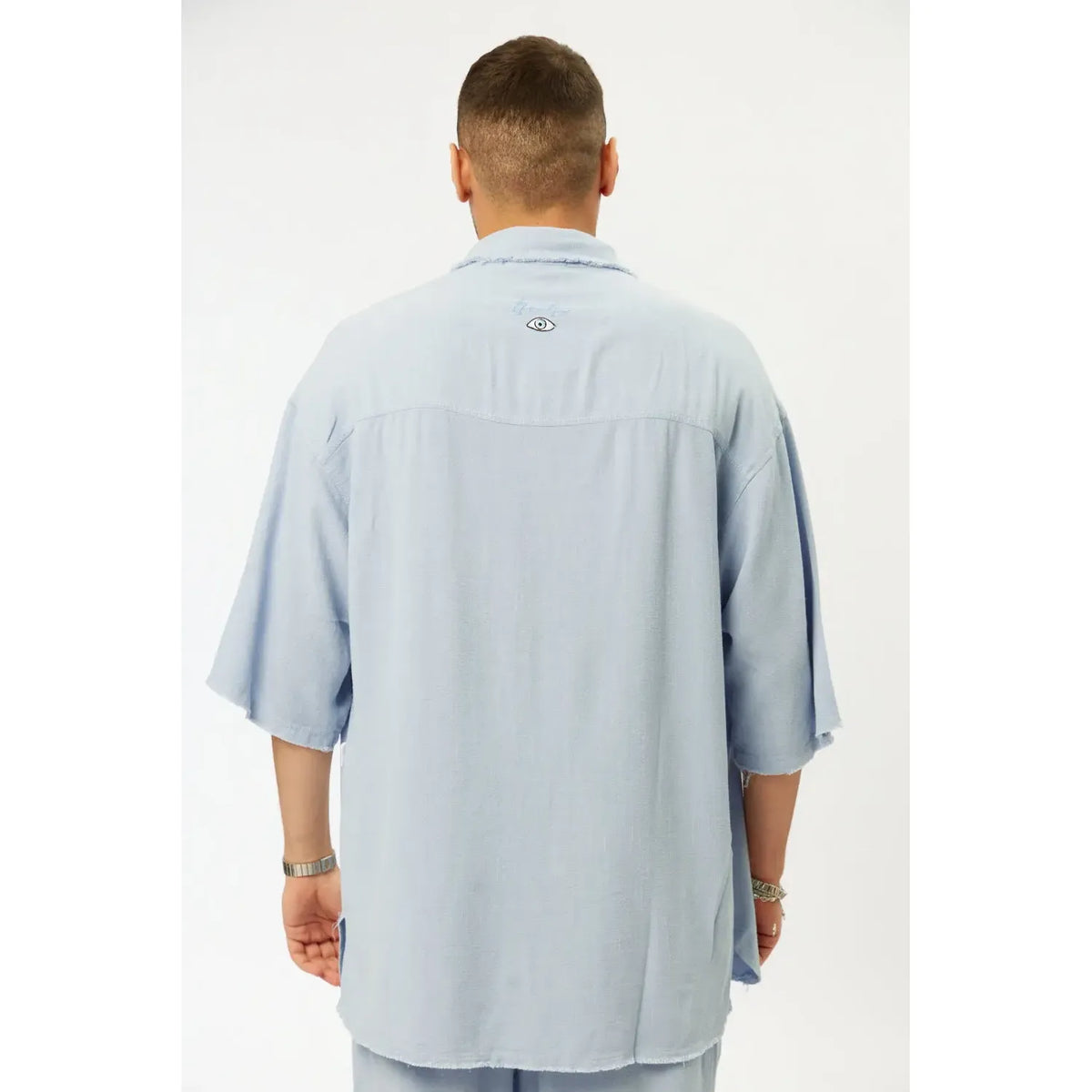 Man wearing a light blue shirt with a brand logo on the back against a white background