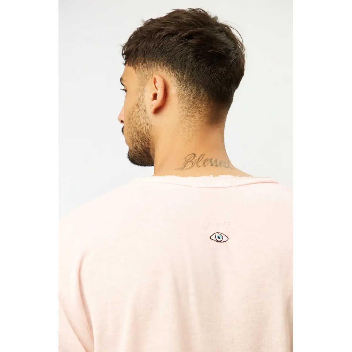 Back of a man wearing a Nicki Soft Open Top in pink, with a small eye graphic and Blessed tattoo on his neck