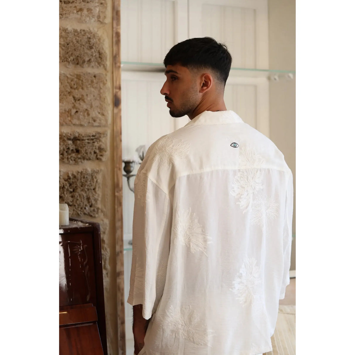 Man wearing a white SPARKS 3/4 Sleeve Button-Up Shirt with embroidered floral patterns and an eye logo on the back