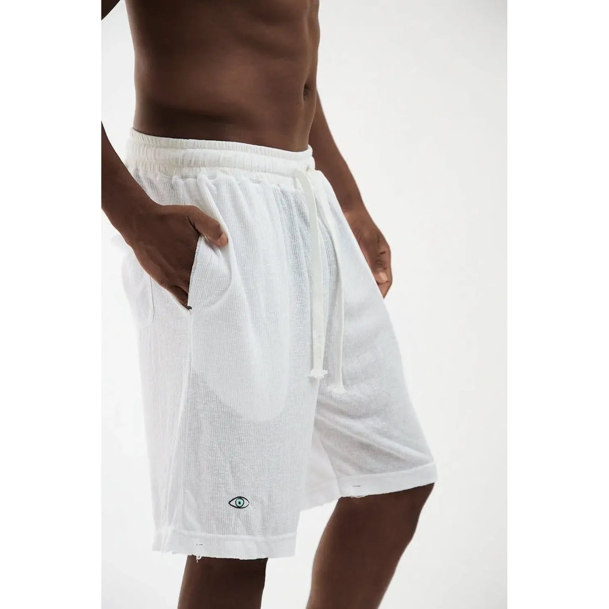 Man wearing white Rib Bermuda Shorts with a drawstring waist and an eye logo on the left leg