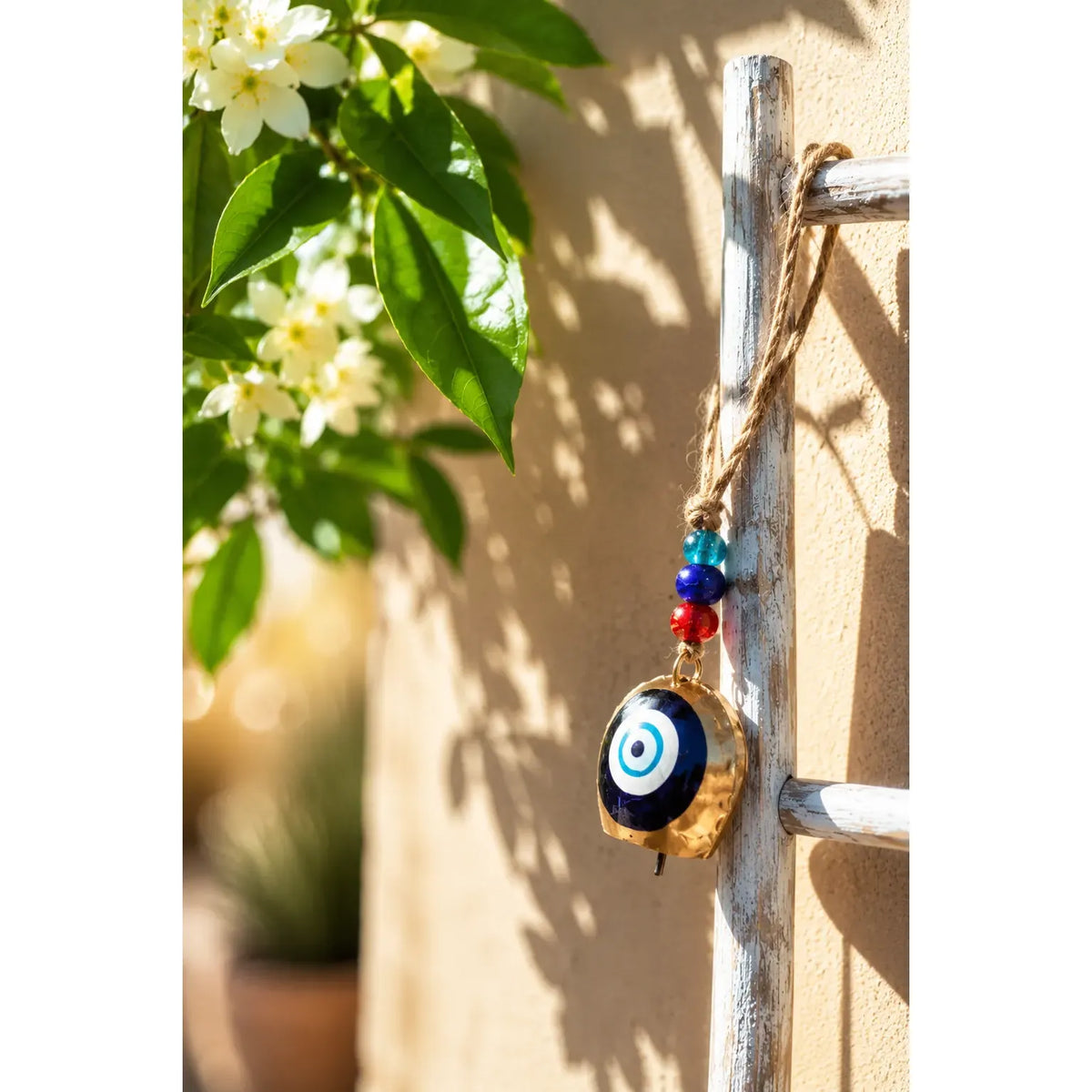 Single Hanging Bell Mobile with a blue evil eye design, red and blue beads, hanging from a rustic white ladder