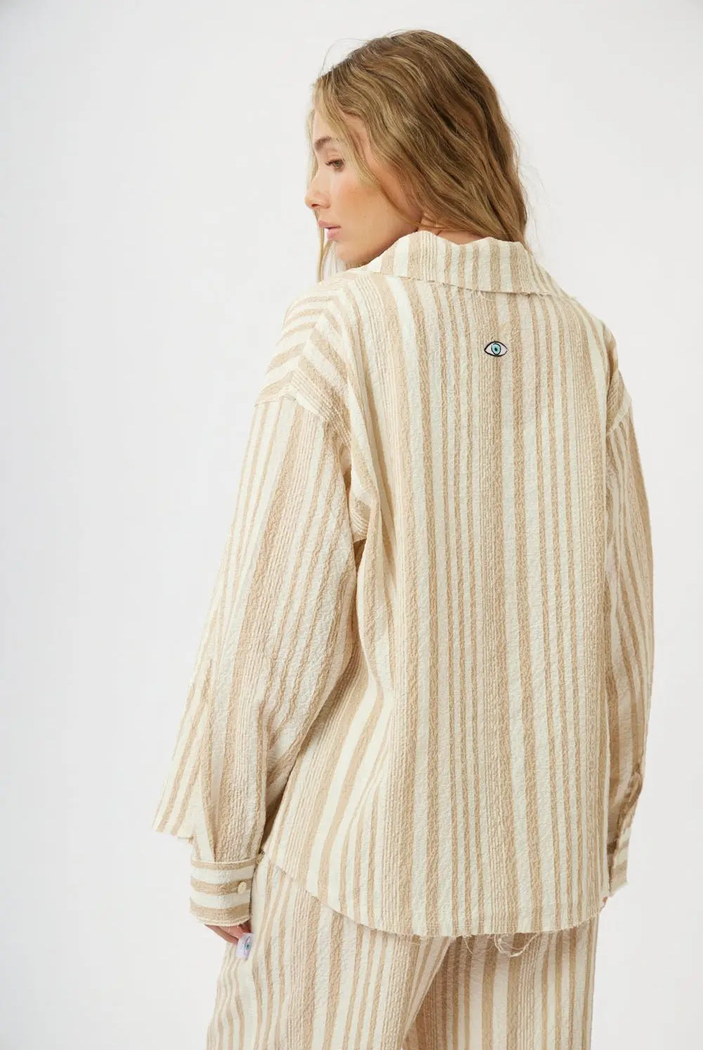 Soft Linen Women's Button-Up Shirt in beige and white stripes, seen from the back with an eye logo on the collar