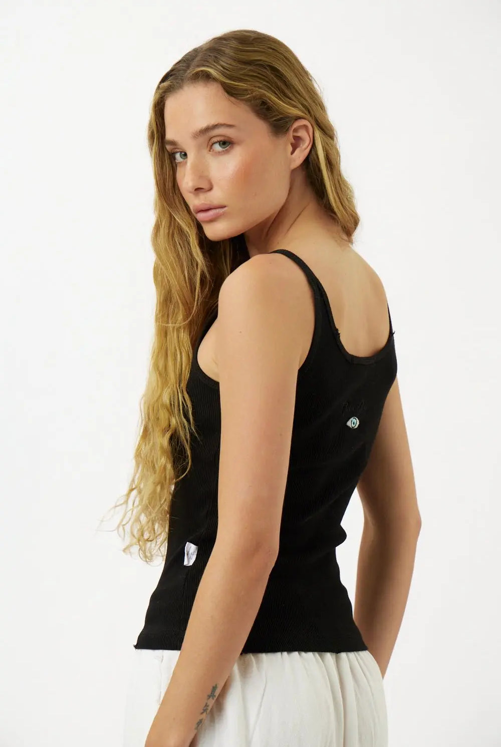 Slim Cotton Tank Top in black, worn by a woman with long blonde hair, looking over her shoulder