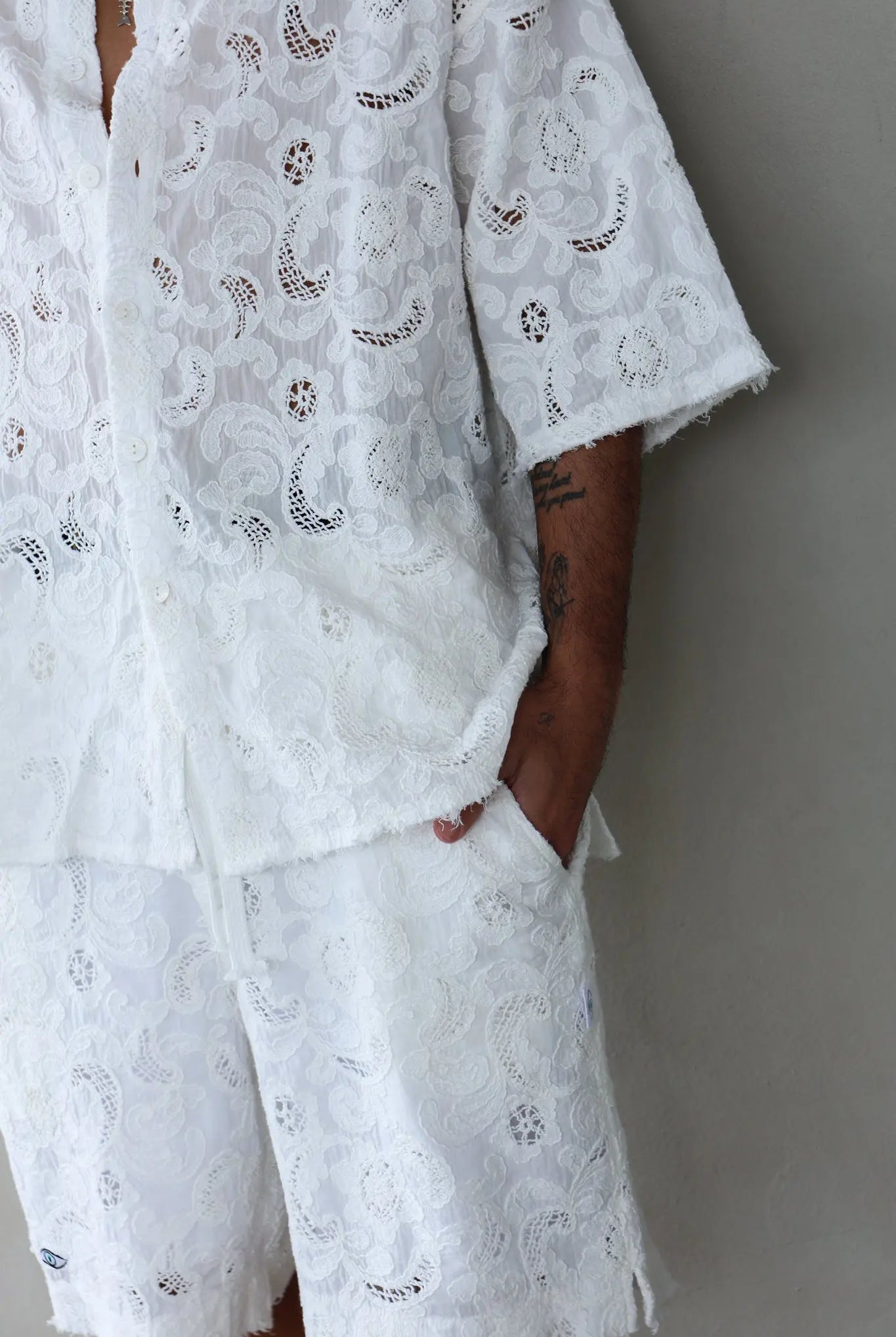 FLR WHITE LIMITED EDITION Shorts, white lace fabric with floral and paisley patterns, worn by a person with a tattooed arm