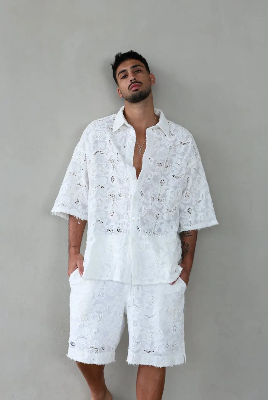 Man wearing a white embroidered shirt and shorts against a gray background