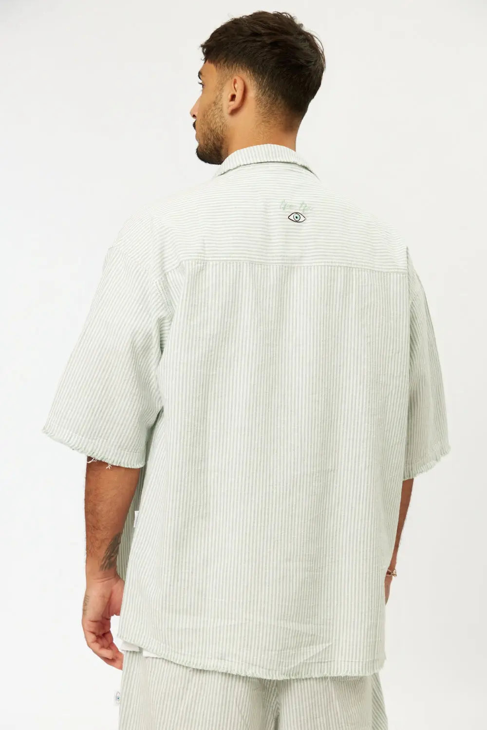Back of a man wearing a Striped Green Linen Set, short sleeve shirt and Bermuda shorts, with an eye graphic on the back of the shirt
