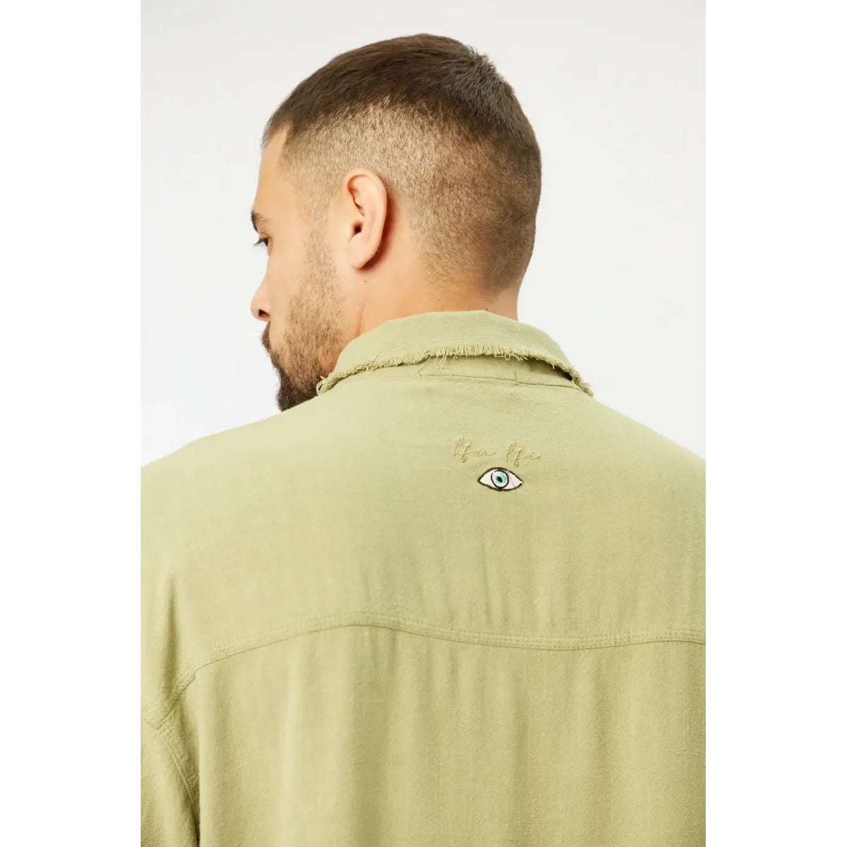 Back of a man wearing a green Soft Linen Short Sleeve Button-Up Shirt with an embroidered eye design