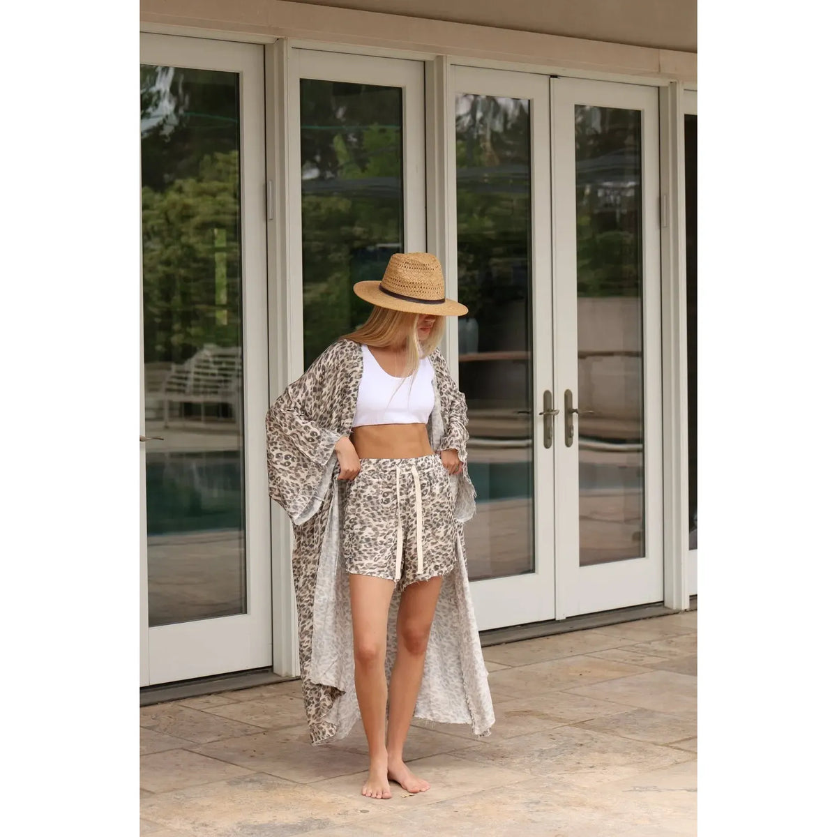 Woman wearing satin leopard shorts, a white crop top, a leopard print kimono, and a straw hat