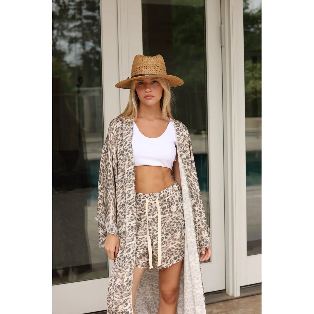 Woman wearing satin leopard shorts, a matching long kimono, a white crop top, and a straw hat
