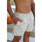 A close-up of a man wearing light beige swim trunks with a multicolor paisley pattern, featuring a drawstring waist and side pockets.