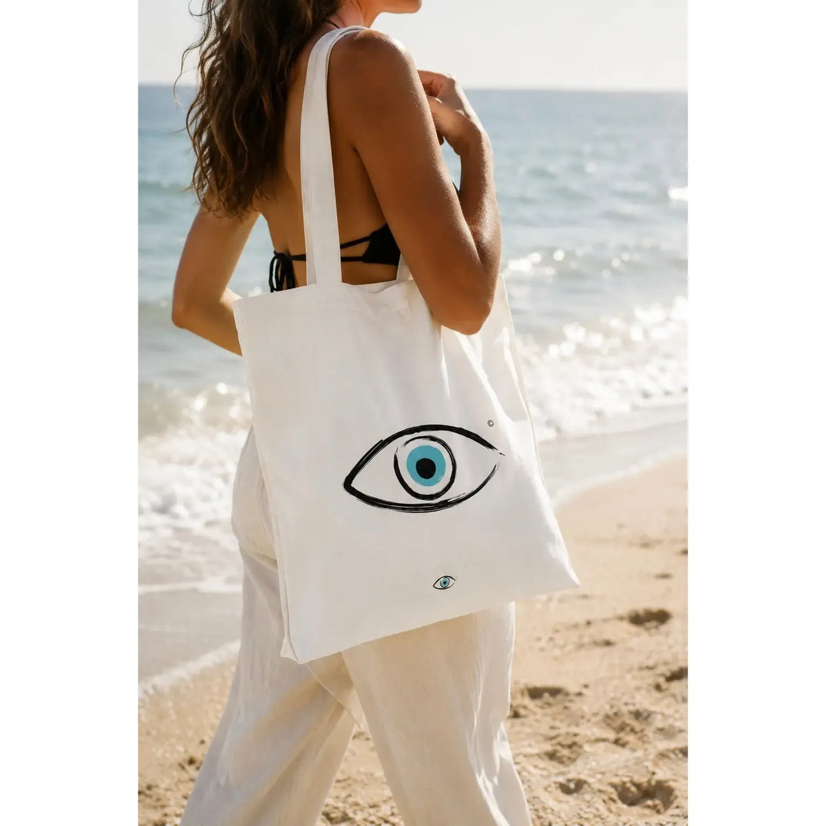 Multi Bag - White with an eye graphic, carried by a person on a beach