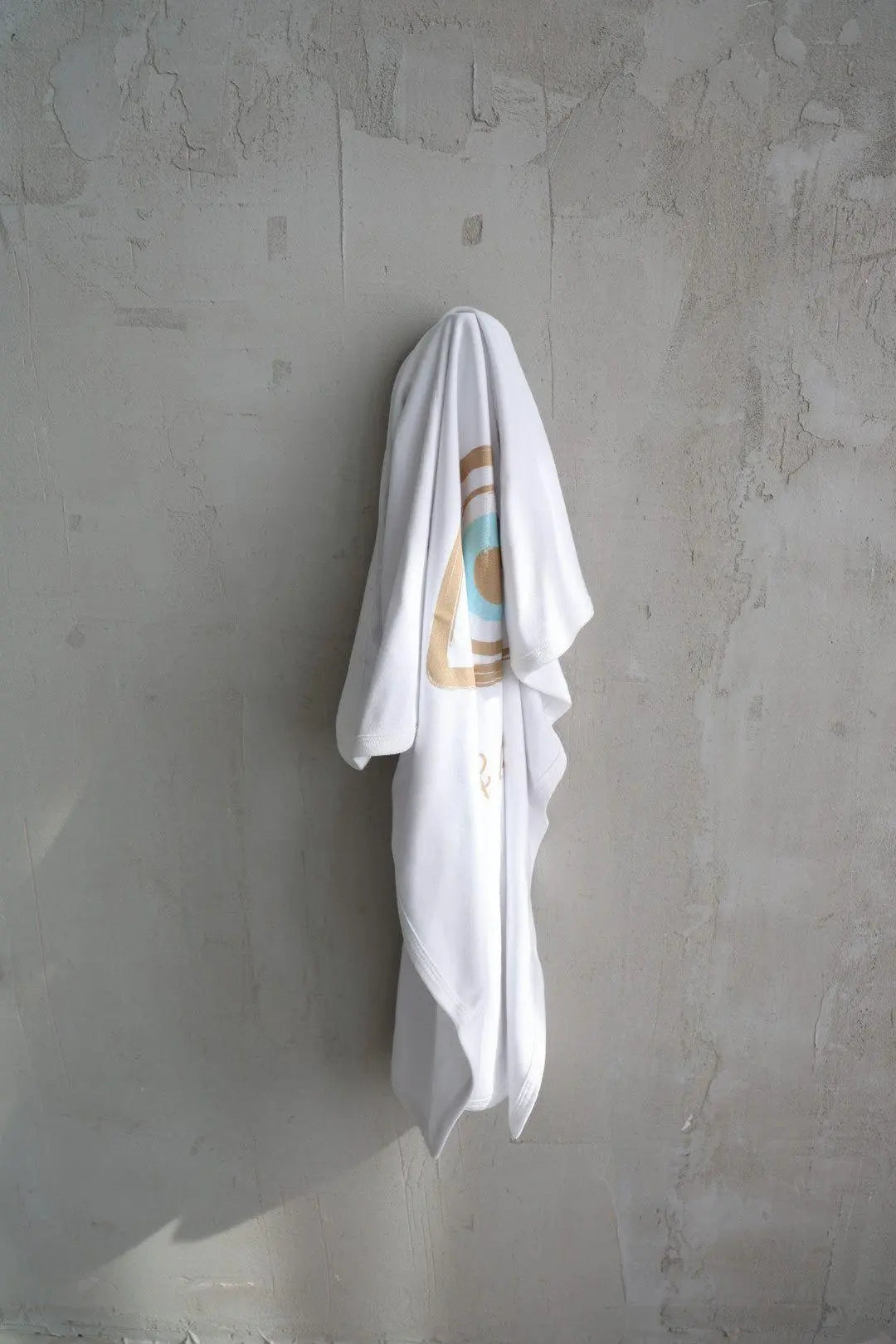 Cotton Single Elliptical Eye Blanket draped over a hook on a textured grey wall