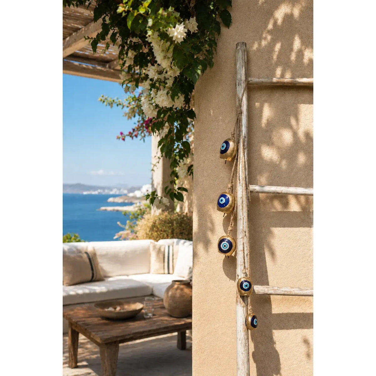 Graduated Bell Mobile (Large to Small) hanging on a wooden ladder against a beige wall, with a patio and ocean in the background