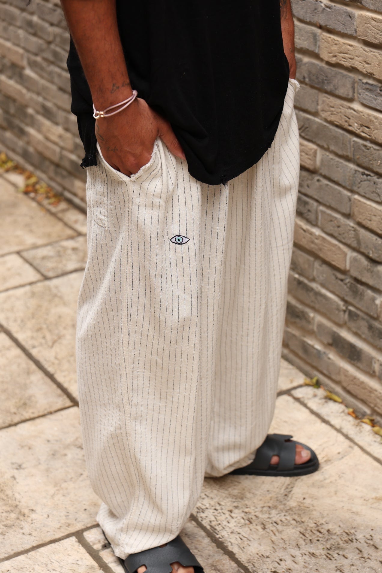 Person wearing white ribbed pants with a brand logo, standing against a brick wall.