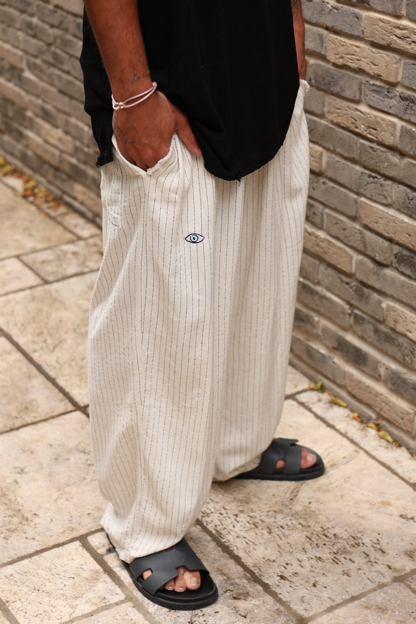 Person wearing light-colored wide-leg pants with a brand logo, standing against a brick wall.