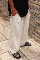 Person wearing light-colored wide-leg pants with a brand logo, standing against a brick wall.
