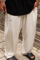 Person wearing beige pants with a small logo, standing on a stone path with a brick wall background.