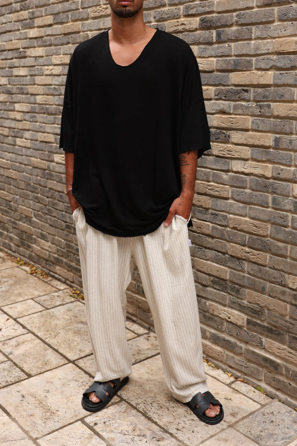 Person wearing a black oversized shirt and white pants standing against a brick wall.