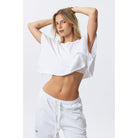 A woman modeling a white cropped t-shirt and matching white sweatpants against a light gray studio background.