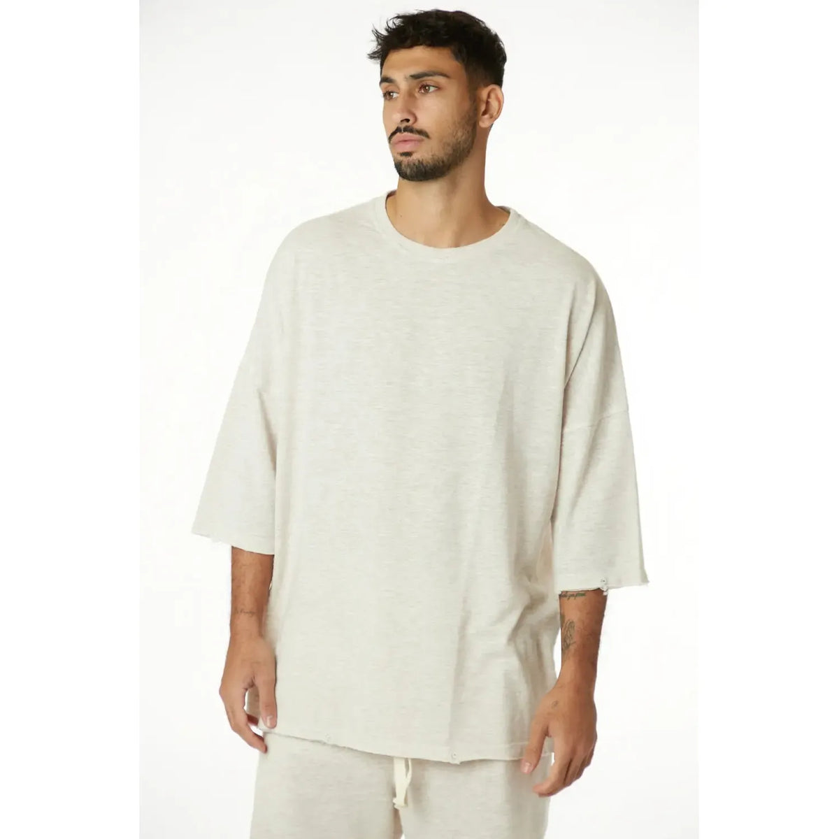 Man wearing a 3/4 Sleeve Nicki Soft in Melange Stone, a light beige oversized t-shirt with raw edges and matching shorts