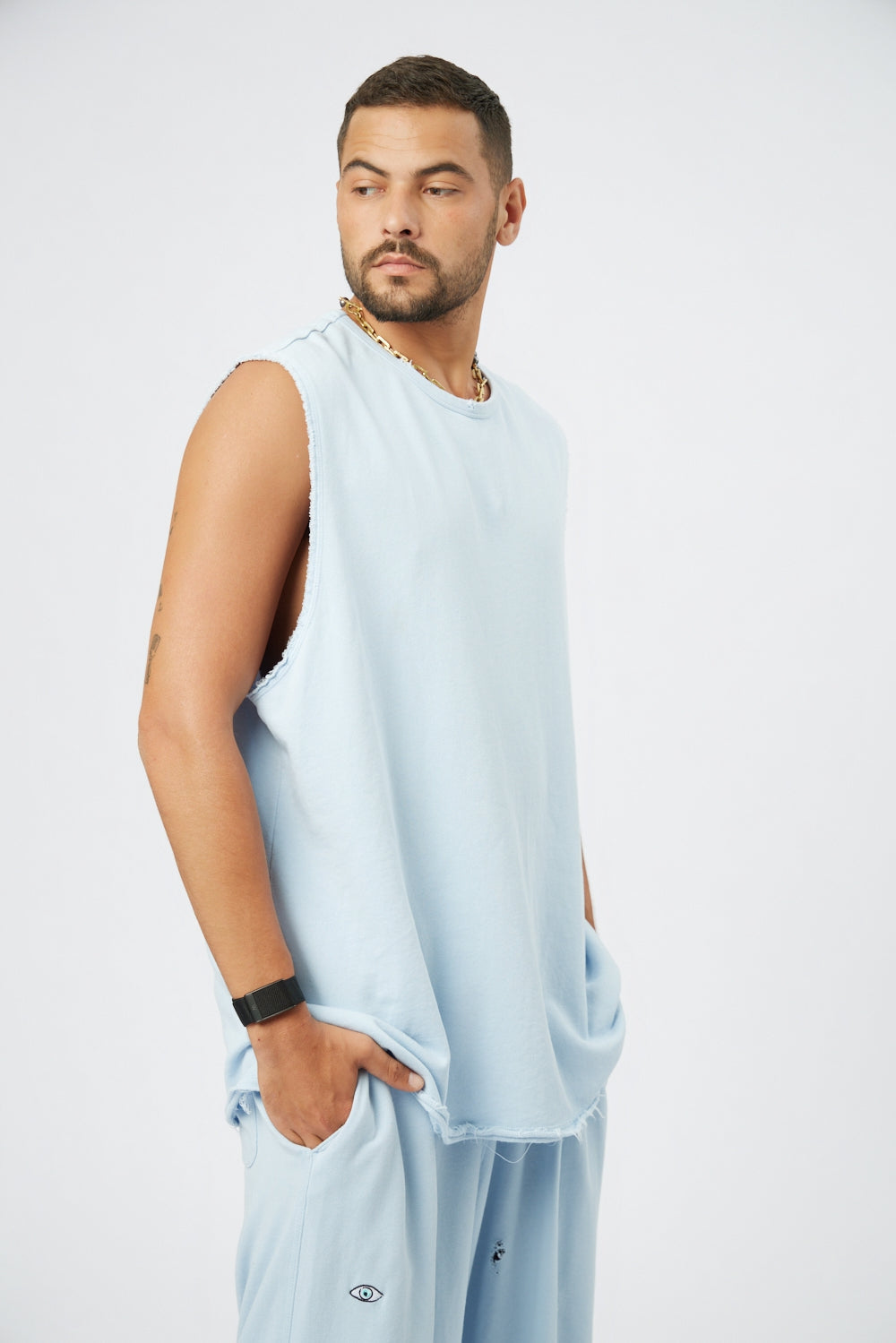 Man wearing a light blue sleeveless shirt and light blue pants on a white background