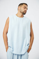 Man wearing a light blue sleeveless top and pants against a white background