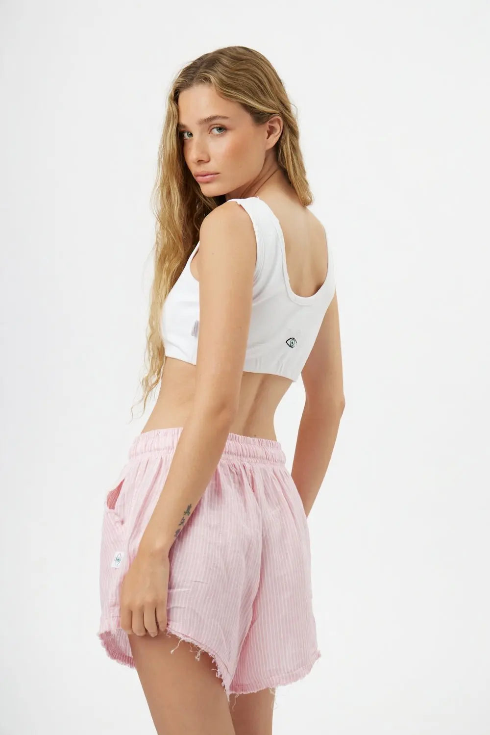 Woman wearing a white crop top and pink shorts on a white background
