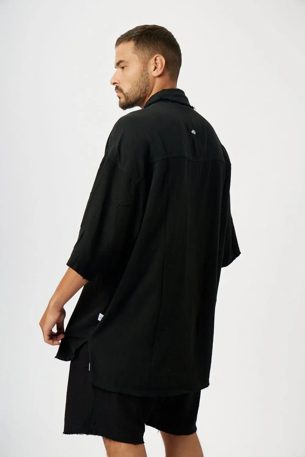 Man wearing a black Soft Linen Short Sleeve Button-Up Shirt and black shorts, viewed from behind