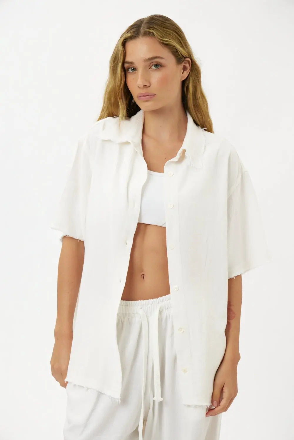 Woman wearing a white Soft Linen Short Sleeve Button-Up Shirt, unbuttoned over a white bralette and white linen shorts