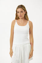 Woman wearing a white tank top and white pants on a white background