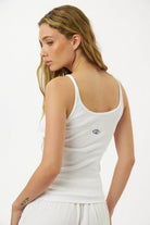 Woman wearing a white tank top with a small logo on a plain background