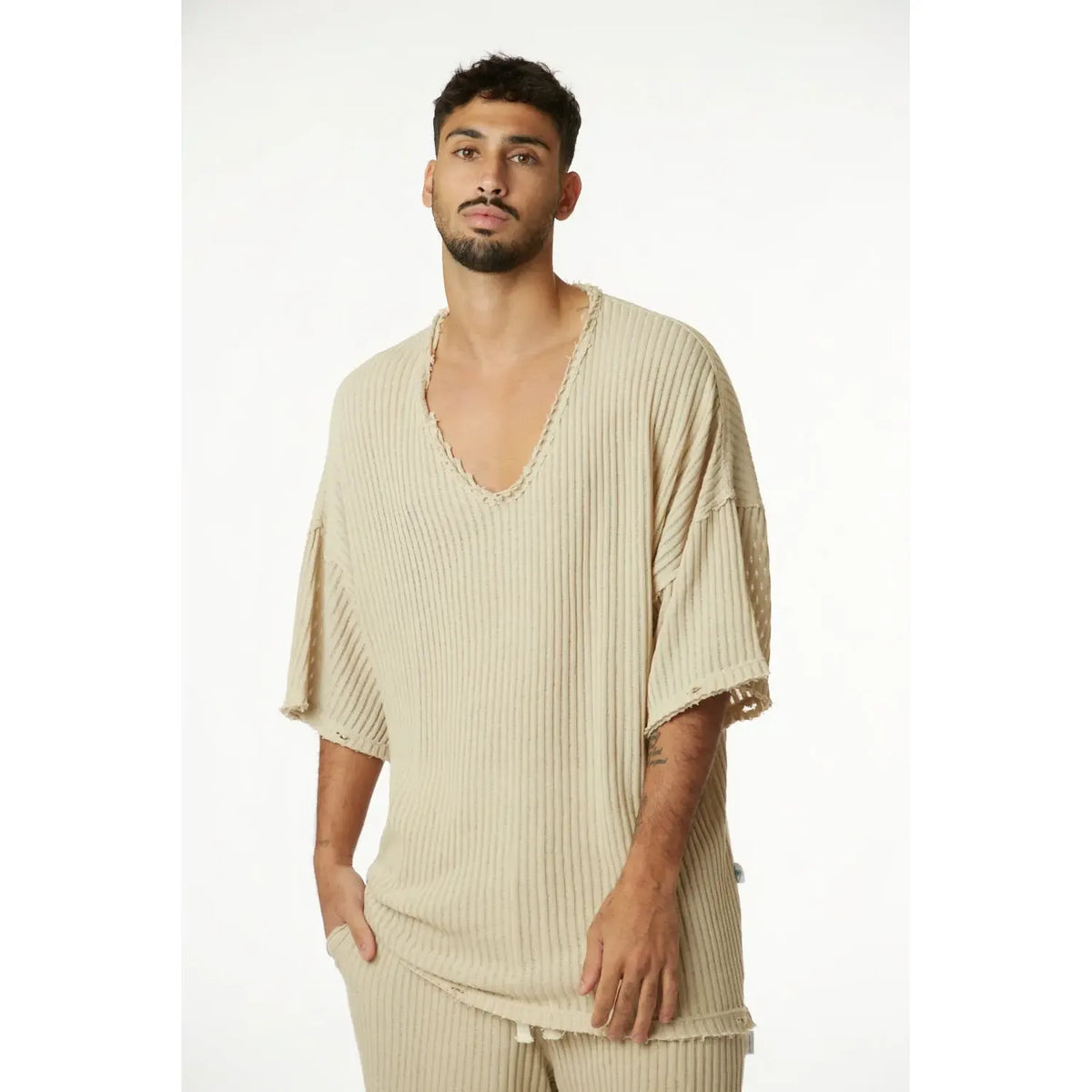 Man wearing a stone striped knit shirt with a deep V-neck and distressed edges