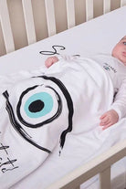 Baby in a crib wearing a white Cotton Single Elliptical Eye Blanket with a large blue and black eye design