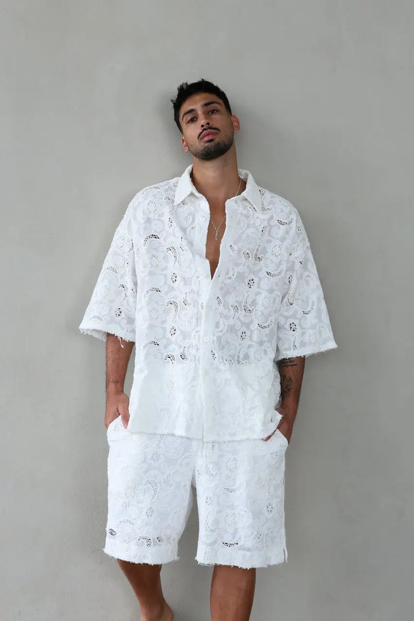Man wearing a white embroidered shirt and shorts against a gray background