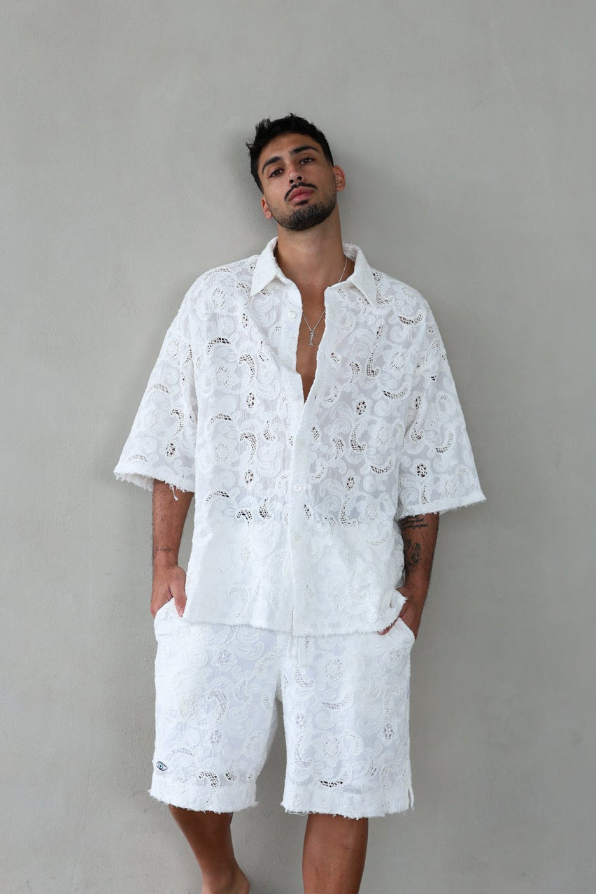Man wearing a white embroidered shirt and shorts against a gray background